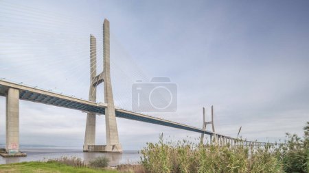 Foto de Architectural landmark Vasco da Gama Bridge over the Tagus River in Lisbon, Portugal. Green grass and cloudy sky. The longest bridge in the European Union. - Imagen libre de derechos