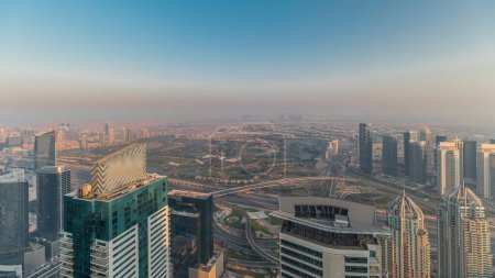 Téléchargez les photos : Panorama de Dubai Marina avec gratte-ciel JLT et parcours de golf timelapse pendant le coucher du soleil, Dubaï, Émirats arabes unis. Vue aérienne depuis les tours supérieures. Skyline de la ville avec des toits - en image libre de droit
