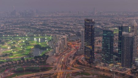 Foto de Gran cruce de caminos entre el distrito JLT y el puerto deportivo de Dubái intersecado por Sheikh Zayed Road día aéreo a noche timelapse transición. Tráfico de coches cerca de rascacielos iluminados - Imagen libre de derechos