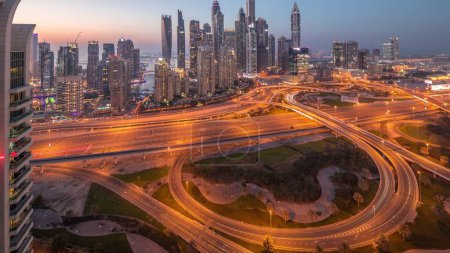 Photo for Panorama of Dubai Marina highway intersection spaghetti junction day to night transition timelapse. Illuminated tallest skyscrapers on a background. Aerial top view from JLT district after sunset - Royalty Free Image