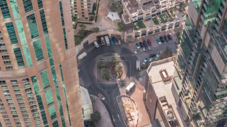 Téléchargez les photos : Vue aérienne vers le bas d'un carrefour routier circulaire entre des gratte-ciel avec des ombres se déplaçant rapidement dans une grande ville. Paysage urbain du quartier Marina de Dubaï aux Émirats Arabes Unis avec voitures et parking près du supermarché - en image libre de droit