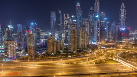 Photo for Skyscrapers of Dubai Marina with illuminated highest residential buildings during all night timelapse with lights turning off. Aerial top view from JLT district. Traffic on a highway - Royalty Free Image