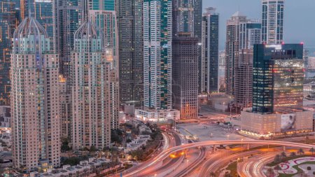 Téléchargez les photos : Les gratte-ciel de Dubai Marina avec les bâtiments résidentiels les plus lumineux du jour au soir après le coucher du soleil. Vue aérienne du quartier JLT avec intersection de l'autoroute - en image libre de droit