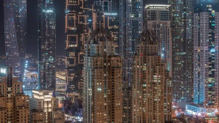 Photo for Skyscrapers of Dubai Marina with illuminated blinking windows on highest residential buildings during all night timelapse. Aerial top view from JLT district - Royalty Free Image