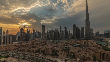 Foto de Puesta de sol sobre Dubai Centro timelapse con más alto rascacielos y otras torres vista desde la parte superior en Dubai, Emiratos Árabes Unidos. Rayos de luz y cielo anaranjado nublado - Imagen libre de derechos