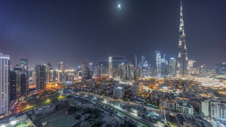 Téléchargez les photos : Dubaï Centre-ville pendant toute la nuit panorama intemporel avec le plus haut gratte-ciel et d'autres tours éclairées vue du haut à Dubaï, Émirats arabes unis. Lune sur le ciel et lumières éteintes - en image libre de droit