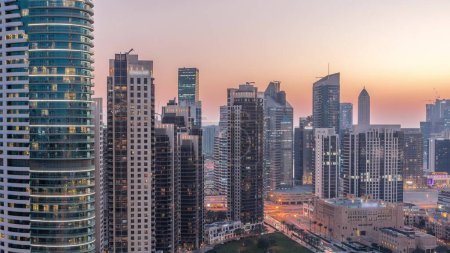 Foto de Bahía de negocios torres aéreas día a noche timelapse transición en Dubai. Vista de la azotea de algunos rascacielos y edificios nuevos en construcción después del atardecer. Luces encendidas - Imagen libre de derechos