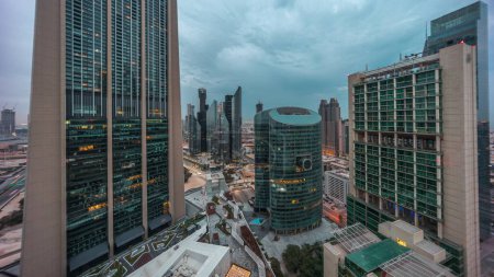 Foto de Dubai centro financiero internacional rascacielos panorama aéreo noche a día timelapse transición. Vista de torres iluminadas desde arriba antes del amanecer con cielo nublado y colorido - Imagen libre de derechos