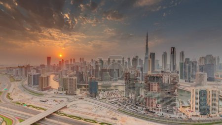 Téléchargez les photos : Skyline avec l'architecture moderne des tours de la baie d'affaires de Dubaï et le centre-ville au coucher du soleil timelapse. Vue panoramique aérienne avec canal et chantier - en image libre de droit