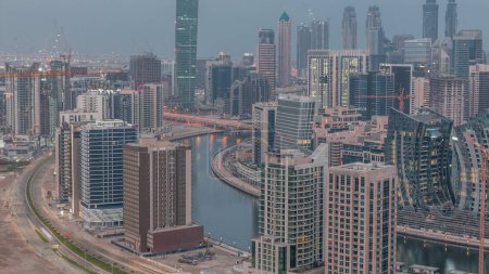Téléchargez les photos : Skyline avec l'architecture moderne de la baie d'affaires de Dubaï illuminé tours nuit à jour timelapse de transition. Vue aérienne avec canal et chantier avant le lever du soleil - en image libre de droit