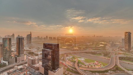 Téléchargez les photos : Lever du soleil sur la jonction de l'autoroute près de la ville des médias et de la zone du quartier al Barsha Heights sur fond de marina de Dubaï. Tours et gratte-ciel tôt le matin avec terrain de golf et circulation sur une autoroute - en image libre de droit