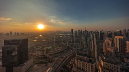 Foto de Salida del sol sobre el puerto deportivo de Dubái y los rascacielos JLT a lo largo del timelapse aéreo de Sheikh Zayed Road. Edificios residenciales y de oficinas desde arriba. Cielo naranja sobre campo de golf - Imagen libre de derechos