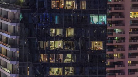 Téléchargez les photos : Fenêtres lumineuses dans les immeubles modernes de bureaux et résidentiels timelapse la nuit. gratte-ciel à plusieurs niveaux avec des pièces éclairées à l'intérieur et des reflets de surface en verre - en image libre de droit