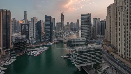 Foto de Vista aérea de los rascacielos y torres de jbr del puerto deportivo de Dubái alrededor del canal con barcos flotantes día a noche timelapse transición. Barcos blancos están estacionados en el club de yates después del atardecer - Imagen libre de derechos