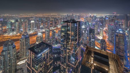 Photo for Dubai Marina and JLT district with traffic on highway between skyscrapers panoramic aerial night timelapse. Illuminated modern towers and construction site - Royalty Free Image