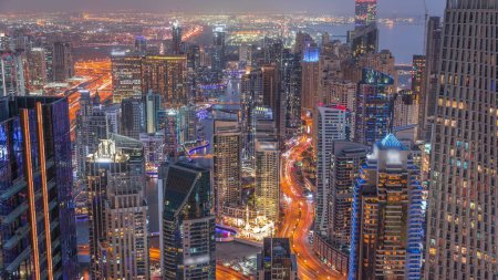 Foto de Vista panorámica del horizonte de Dubai Marina y JBR que muestra el canal rodeado de rascacielos iluminados a lo largo de la costa día aéreo a la transición nocturna. Tráfico en carretera curva después del atardecer. DUBAI, Emiratos Árabes Unidos - Imagen libre de derechos