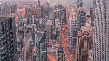 Foto de Vista panorámica del puerto deportivo de Dubái que muestra el canal rodeado de rascacielos iluminados a lo largo del timelapse de transición de noche a día. Yates flotantes y tráfico por carretera antes del amanecer. DUBAI, Emiratos Árabes Unidos - Imagen libre de derechos