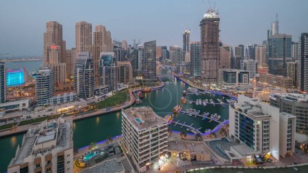 Foto de Dubai Marina con varios barcos y yates estacionados en el puerto y rascacielos alrededor del canal aéreo día a noche timelapse transición. Torres del distrito JBR y obras de construcción con grúas - Imagen libre de derechos