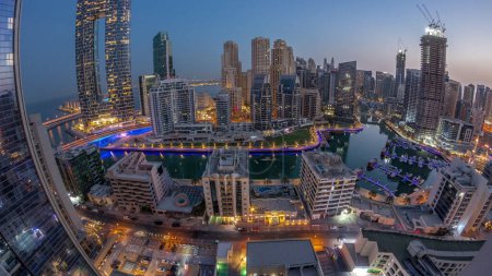 Foto de Panorama de Dubai Marina con barcos y yates aparcados en el puerto y rascacielos iluminados alrededor del canal aéreo noche al día timelapse transición antes del amanecer. Torres del distrito JBR en segundo plano - Imagen libre de derechos