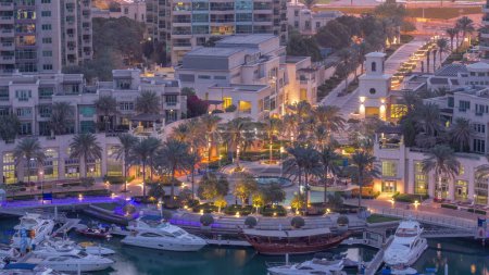 Téléchargez les photos : Fontaine pittoresque sur Dubai Marina promenade aérienne nuit au jour passage timelapse avec palmier autour et yachts dans le port avant le lever du soleil - en image libre de droit