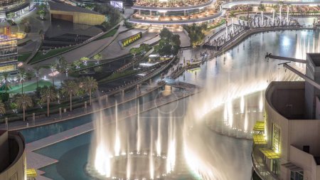 Téléchargez les photos : Dubai promenade chantant fontaines sur le fond de l'architecture aérienne timelapse. Les gens regardent le spectacle près du centre commercial - en image libre de droit