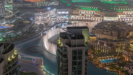 Photo for Dubai promenade singing fountains on the background of architecture with raditional houses in old town aerial timelapse. People watching show near shopping mall - Royalty Free Image