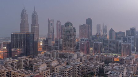 Téléchargez les photos : Des gratte-ciel dans le quartier de Barsha Heights et des immeubles de faible hauteur dans le quartier des Verts se succèdent de nuit au jour. Dubai skyline avec internet ville couverte de brouillard matinal - en image libre de droit
