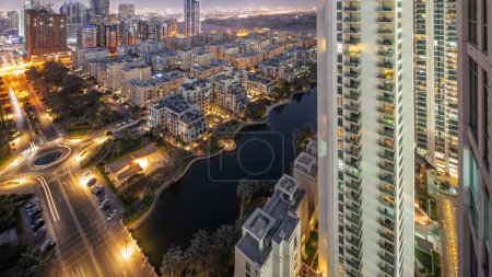 Foto de Estanque y edificios de poca altura en Greens distrito aéreo día a noche timelapse transición. Dubai skyline con rascacielos en el distrito de Barsha Heights en un segundo plano - Imagen libre de derechos