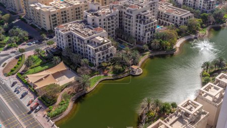 Photo for Pond with fountain and low rise buildings in Greens district aerial timelapse. Dubai skyline with palms and trees. Shadows moving fast - Royalty Free Image
