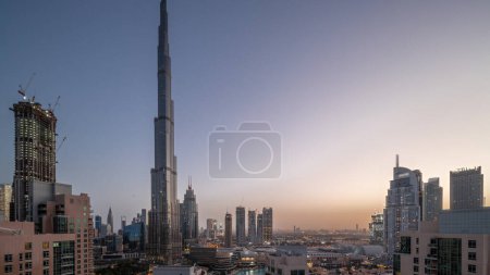 Photo for Dubai Downtown panoramic cityscape with tallest skyscrapers around aerial night to day transition timelapse. Construction site of new towers and busy roads with traffic from above - Royalty Free Image