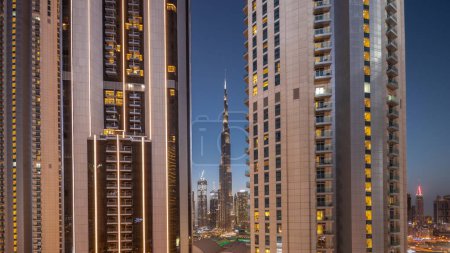 Téléchargez les photos : Les plus hauts gratte-ciel du centre-ville de Dubai situé sur la rue bouleward près du centre commercial aérien jour à la nuit transition timelapse. Fenêtres incandescentes dans les tours après le coucher du soleil - en image libre de droit