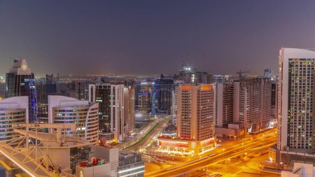 Téléchargez les photos : Des gratte-ciels à Business Bay à Dubaï se succèdent de jour comme de nuit. Carrefour routier et chantier de construction de nouvelles tours avec grues après le coucher du soleil, Émirats arabes unis - en image libre de droit