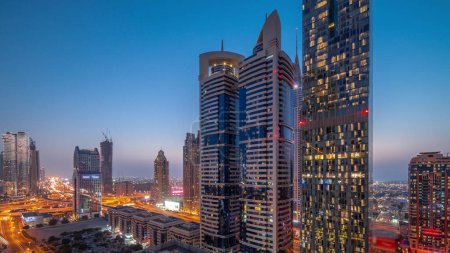 Téléchargez les photos : Vue aérienne du quartier financier international de Dubaï avec de nombreux gratte-ciel de jour comme de nuit après le coucher du soleil. Trafic sur un carrefour routier près du parking. Dubai, Émirats arabes unis. - en image libre de droit