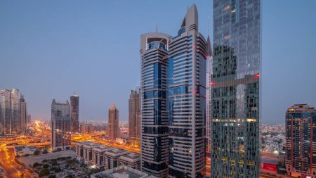 Foto de Vista aérea del Distrito Financiero Internacional de Dubái con muchos rascacielos noche a día timelapse transición. Tráfico en un cruce de carreteras en la carretera Sheikh Zayed antes del amanecer. Dubai, Emiratos Árabes Unidos. - Imagen libre de derechos