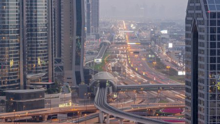 Foto de Ocupado Sheikh Zayed Camino aéreo día a noche timelapse transición, metro ferrocarril y rascacielos modernos alrededor en la ciudad de lujo de Dubai. Tráfico pesado en una carretera con muchos coches. Emiratos Árabes Unidos - Imagen libre de derechos