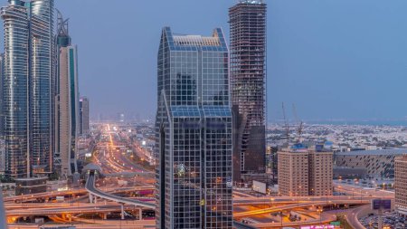 Photo for Dubai city skyline panoramic view with metro and cars moving on city's busiest highway aerial night to day transition timelapse. Junction surrounded by skyscrapers before sunrise - Royalty Free Image