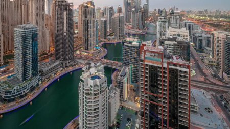 Téléchargez les photos : Vue de divers gratte-ciels dans le plus haut bloc recidential de Dubai Marina aérienne de jour à la nuit timelapse de transition avec canal artificiel et des ponts sur elle. Nombreuses tours et yachts après le coucher du soleil - en image libre de droit