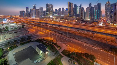 Téléchargez les photos : Dubai Marina gratte-ciel et Sheikh Zayed route avec métro ferroviaire aérien jour à nuit transition timelapse panoramique. Trafic sur une autoroute près des tours modernes après le coucher du soleil, Émirats arabes unis - en image libre de droit