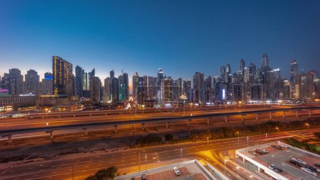 Foto de Panorama de Dubai marina bloque más alto de rascacielos día a noche timelapse transición. Vista aérea desde el distrito JLT a edificios de apartamentos, hoteles y torres de oficinas cerca de la autopista. - Imagen libre de derechos