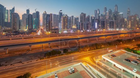 Téléchargez les photos : Dubai Marina plus haut bloc de gratte-ciel jour à nuit passage timelapse. Vue panoramique aérienne du quartier JLT vers les immeubles d'appartements, les hôtels et les tours de bureaux près de l'autoroute et de la ligne de métro. - en image libre de droit