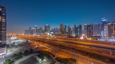 Foto de Dubai Marina rascacielos panorama y Sheikh Zayed carretera con metro tren aéreo día a noche timelapse transición. Tráfico en una autopista cerca de torres modernas después del atardecer, Emiratos Árabes Unidos - Imagen libre de derechos