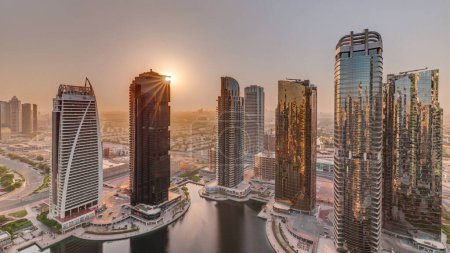 Foto de Salida del sol sobre edificios residenciales altos en el timelapse aéreo del distrito JLT, parte del distrito de uso mixto del centro de productos básicos de Dubai. Rascacielos alrededor del estanque - Imagen libre de derechos