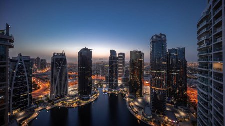 Téléchargez les photos : Panorama des grands bâtiments résidentiels du quartier JLT - passage aérien de nuit au jour - qui fait partie du quartier mixte du centre multi-commodités de Dubaï. Tours et gratte-ciel éclairés - en image libre de droit