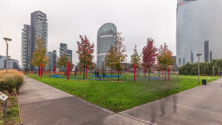 Foto de Panorama showing skyscrapers and biblioteca from park with green lawn and orange trees timelapse. Located between Piazza Gae Aulenti and Isola district. Traffic on a road intersection. Milan. Italy - Imagen libre de derechos