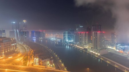 Téléchargez les photos : Architecture moderne de la ville dans le quartier Business Bay pendant toute la nuit. Vue aérienne panoramique des gratte-ciel illuminés de Dubaï avec circulation sur la route. Météo brumeuse et lever du soleil - en image libre de droit