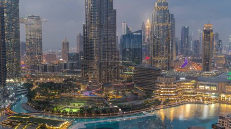 Téléchargez les photos : Gratte-ciel s'élevant au-dessus du centre-ville de Dubaï transition de jour à la nuit, centre commercial et fontaine entourés de bâtiments modernes vue aérienne avec ciel nuageux coloré - en image libre de droit