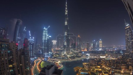 Photo for Skyscrapers rising above Dubai downtown during all night  with lights turning off, mall and fountain surrounded by modern buildings aerial top panoramic view with clouds - Royalty Free Image