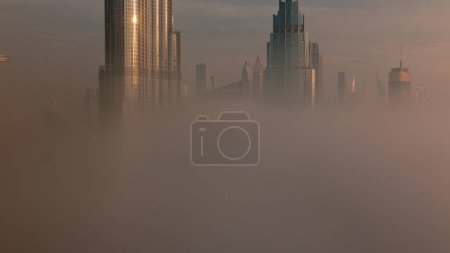 Téléchargez les photos : Aerial view of Dubai city early morning during fog . Sunrise at futuristic city skyline with skyscrapers and towers from above. Sun reflected from glass surface - en image libre de droit