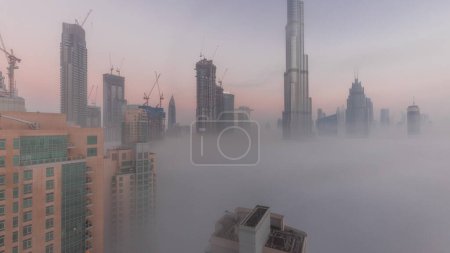 Téléchargez les photos : Aerial view of Dubai city early morning during fog night to day . Futuristic city skyline with skyscrapers and towers under construction from above - en image libre de droit