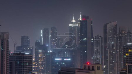 Photo for Dubai skyscrapers with illumination in business bay district during all night . Aerial view with fog from top of downtown in United Arab Emirates. Lights turning off - Royalty Free Image